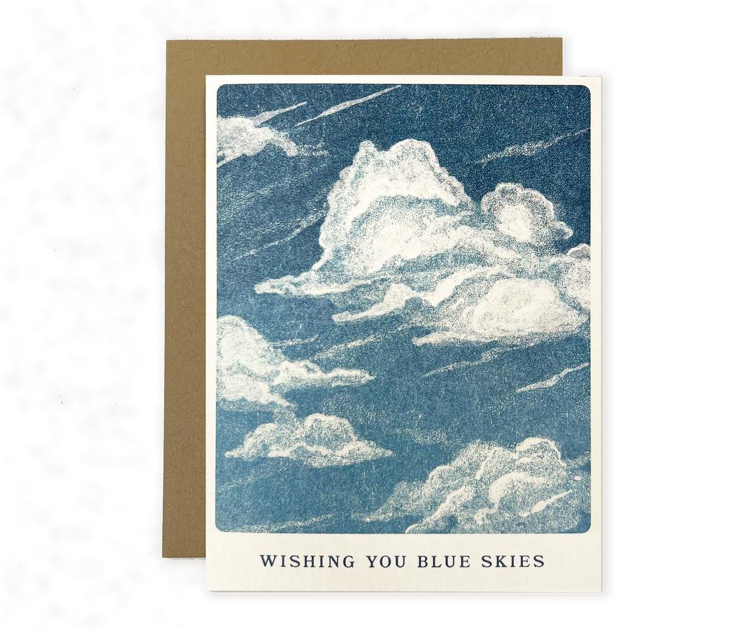 Greeting card with a drawing of white clouds in a blue sky and the text "Wishing You Blue Skies" at the bottom, paired with a brown envelope.