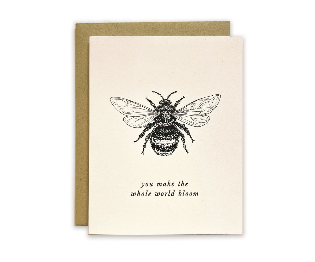 A card with an illustration of a bee and the words &quot;You Make the Whole World Bloom&quot; by The Wild Wander.