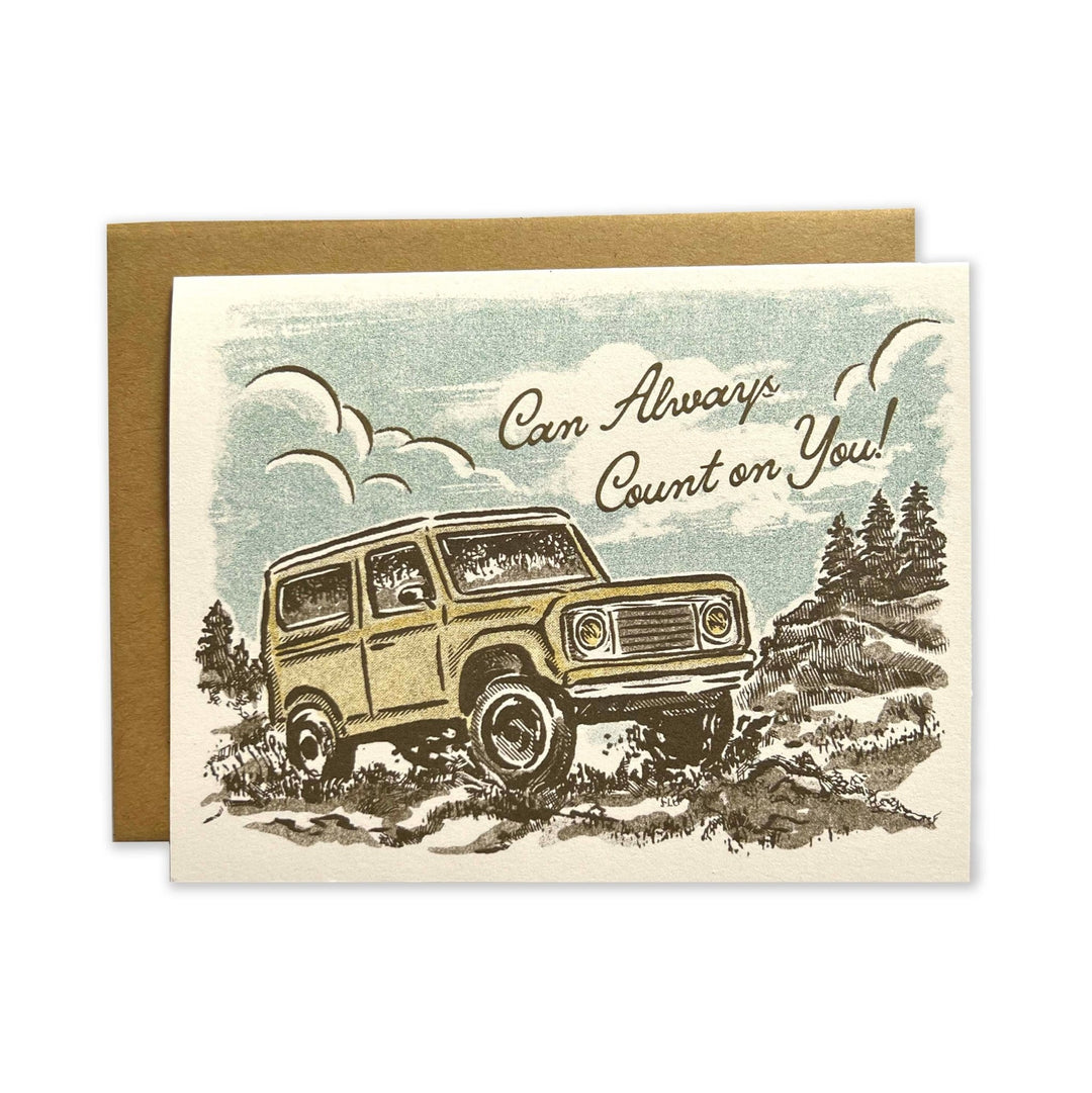 Happy Trails Mountains Greeting Card from The Wild Wander features a vintage illustration of an off-road vehicle on rugged terrain, with the caption "Can Always Count on You!" in cursive text. Crafted from heavyweight cardstock, the card is blank inside for your personal message and comes with a plain brown envelope placed behind it.