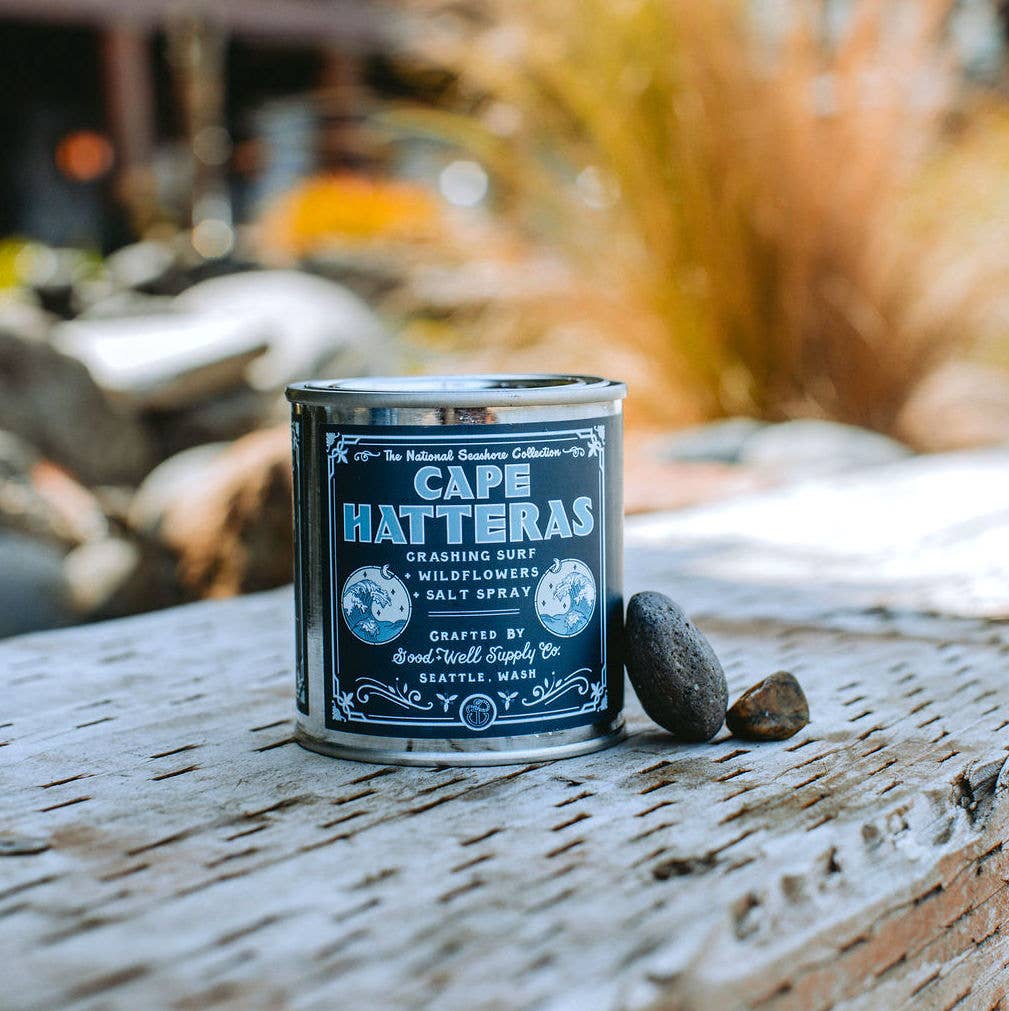 A tin of Cape Hatteras - National Seashores Candle by Good &amp; Well Supply Co. sitting on a wooden table.