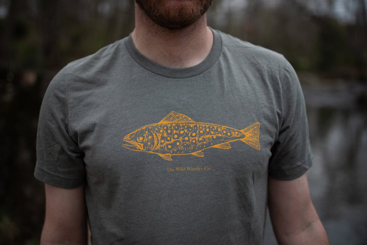 A man wearing a gray Brook Trout T-Shirt with The Wild Wander brand on it.