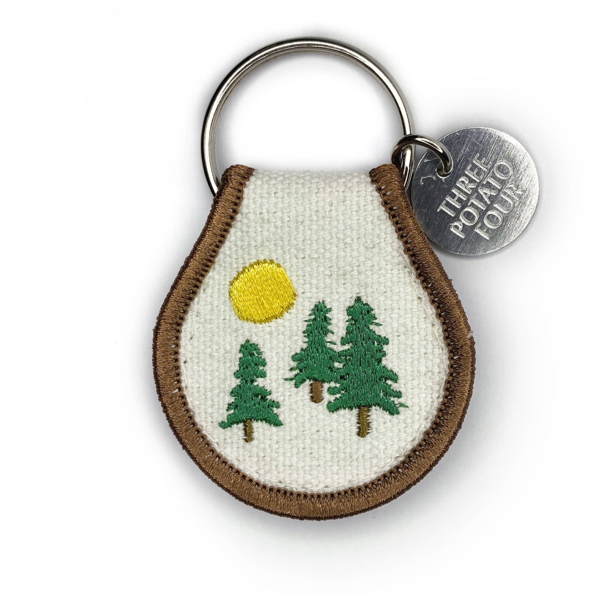 A Patch Keychain - Evergreen by Three Potato Four with a picture of trees and a sun.