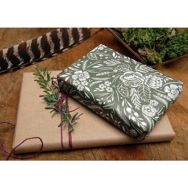 A Wild Wander Gift Card, wrapped in brown paper with a feather and sprigs of ivy.