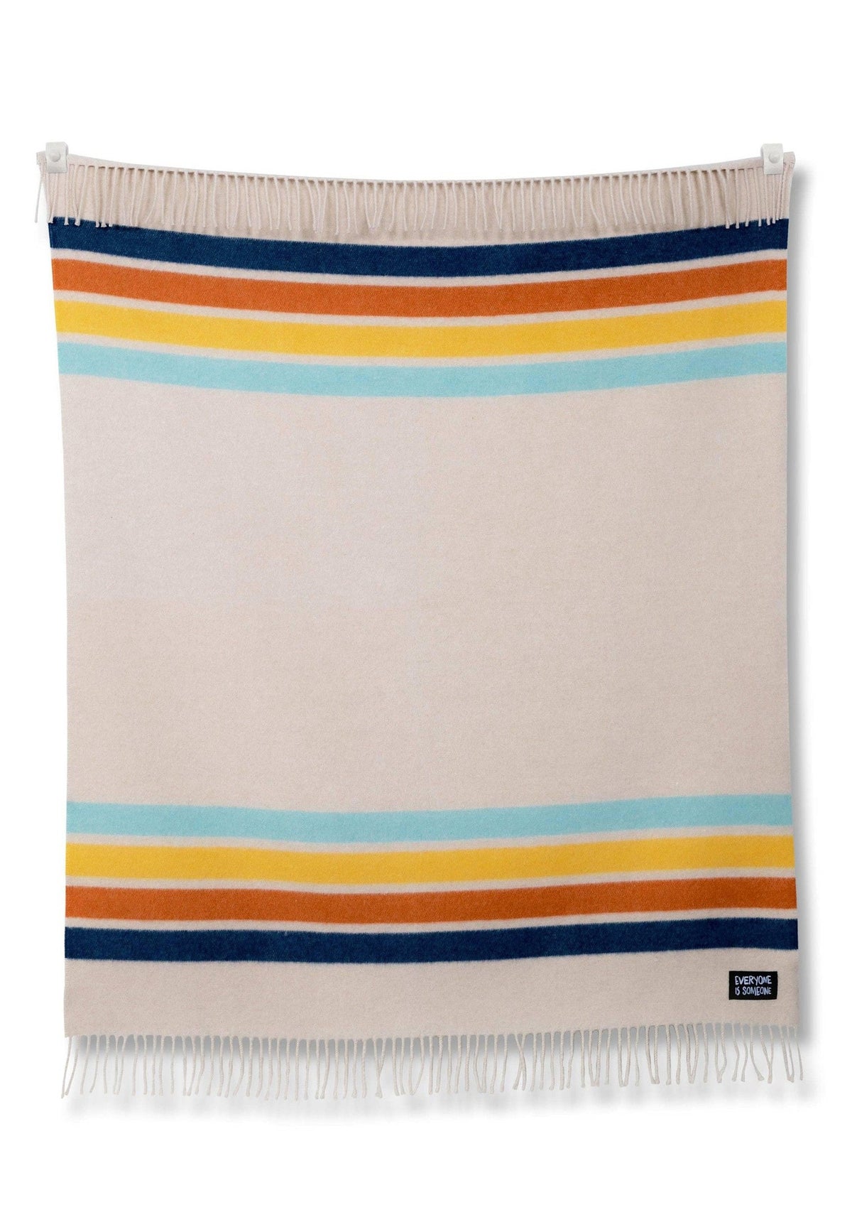 A beige and blue striped KIDS Camp Coast blanket hanging on a white wall by Sackcloth &amp; Ashes.