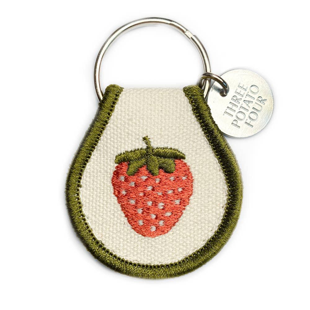 A Patch Keychain - Strawberry with a Three Potato Four embroidered on it.