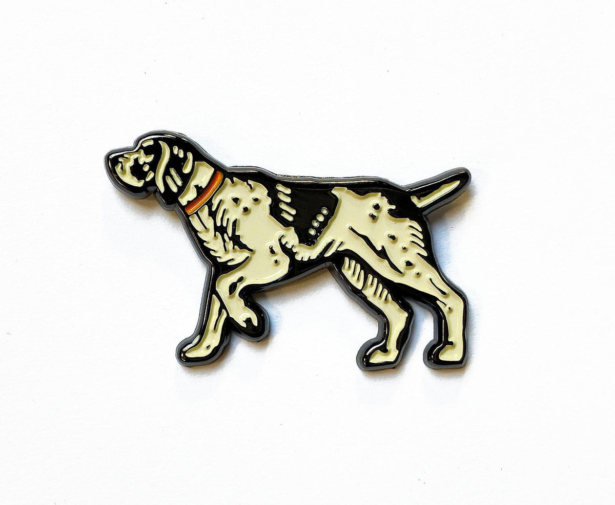 An enamel pin with a Pointer Enamel Pin from The Wild Wander on it.