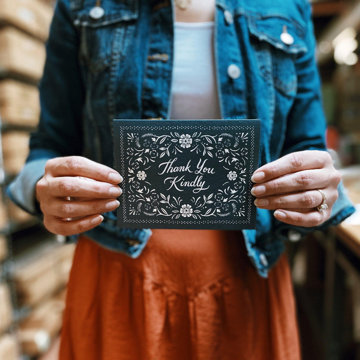 A woman holding up a Thank You Kindly Floral Bandana Card from The Wild Wander in a warehouse.